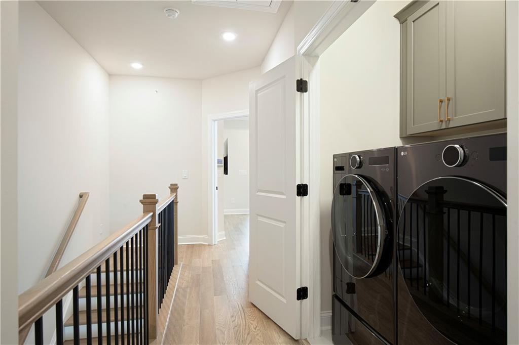 Upstairs laundry area with dark front-loading washer and dryer beneath gray cabinets beside a stair railing.