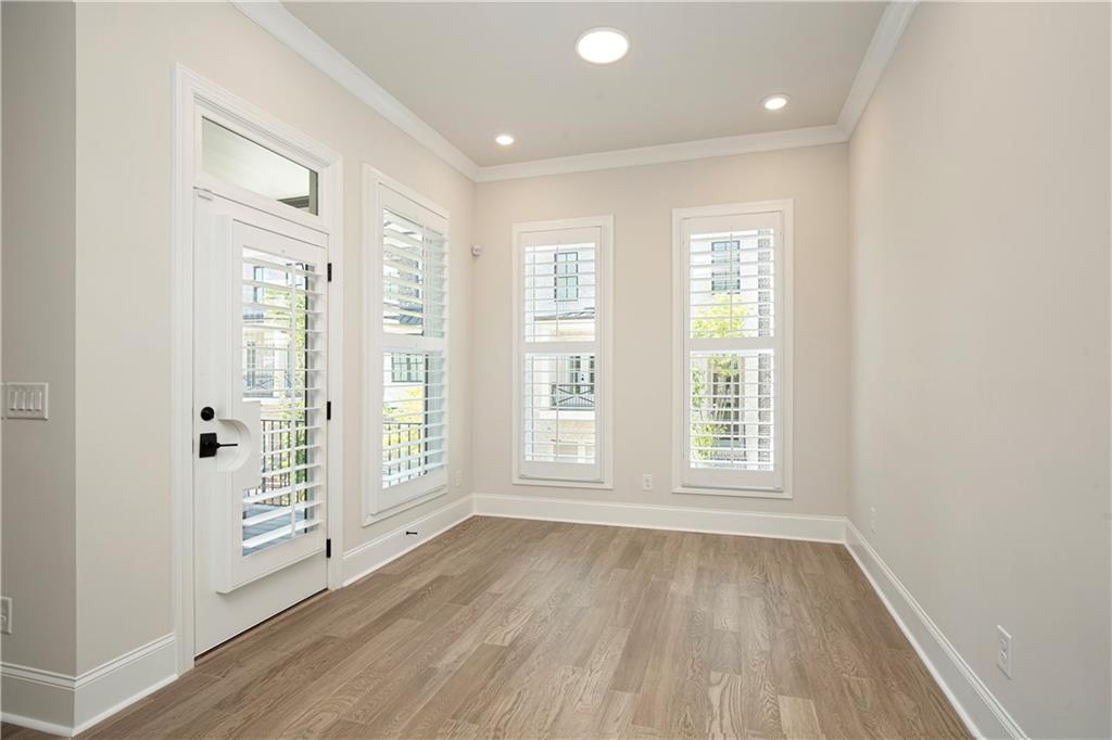 Vacant room with light wood floors, plantation shutters, and a glass-paneled exterior door.