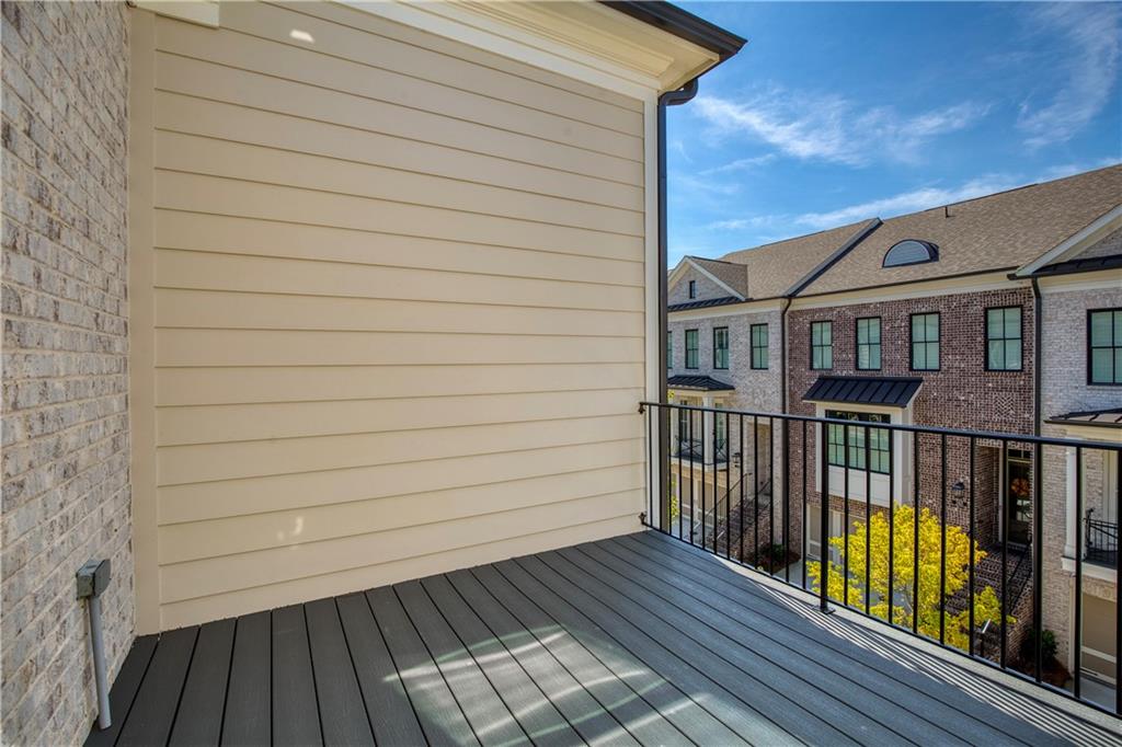 Covered balcony with dark composite decking and black railing overlooking neighboring brick townhomes.