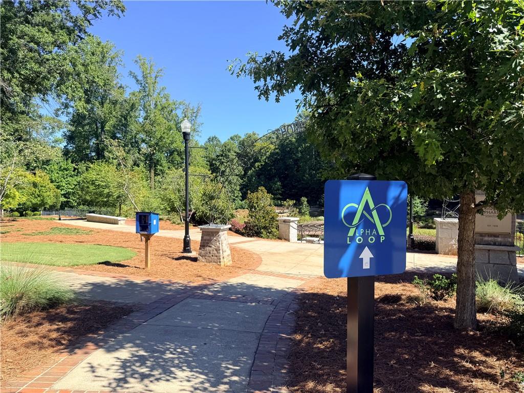 Alpha Loop entrance sign beside a landscaped paved path shaded by trees.