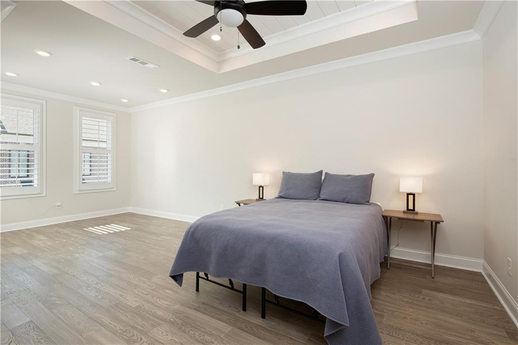 Bedroom with a tray ceiling, ceiling fan, wood flooring, and shuttered windows.