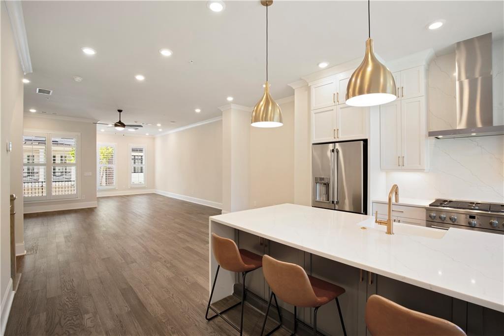 Open-plan kitchen with a large white island, brass pendant lights, and an adjoining empty living area.