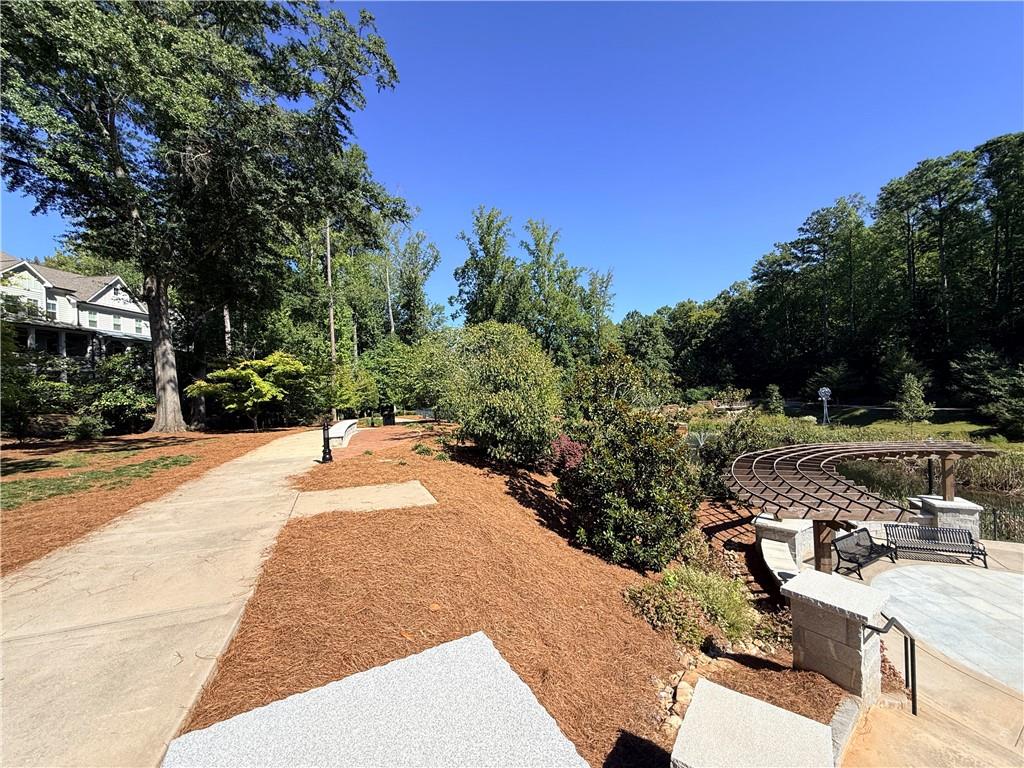 Landscaped yard with a winding walkway, curved pergola, stone patio, and pond.