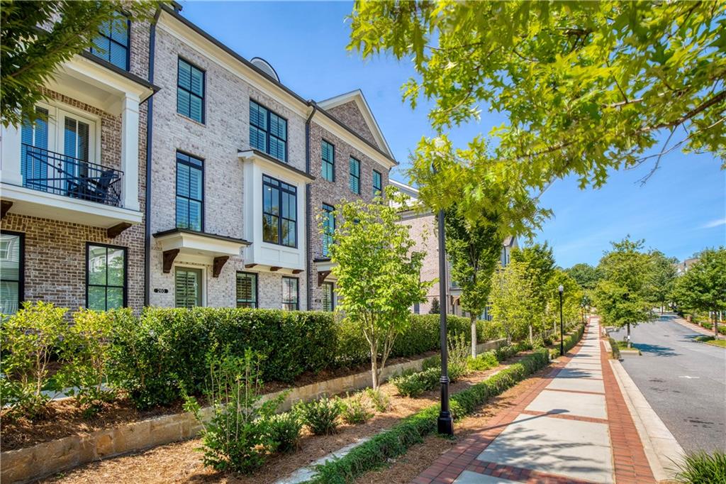 Brick townhome with black-framed windows and balconies beside a landscaped sidewalk.