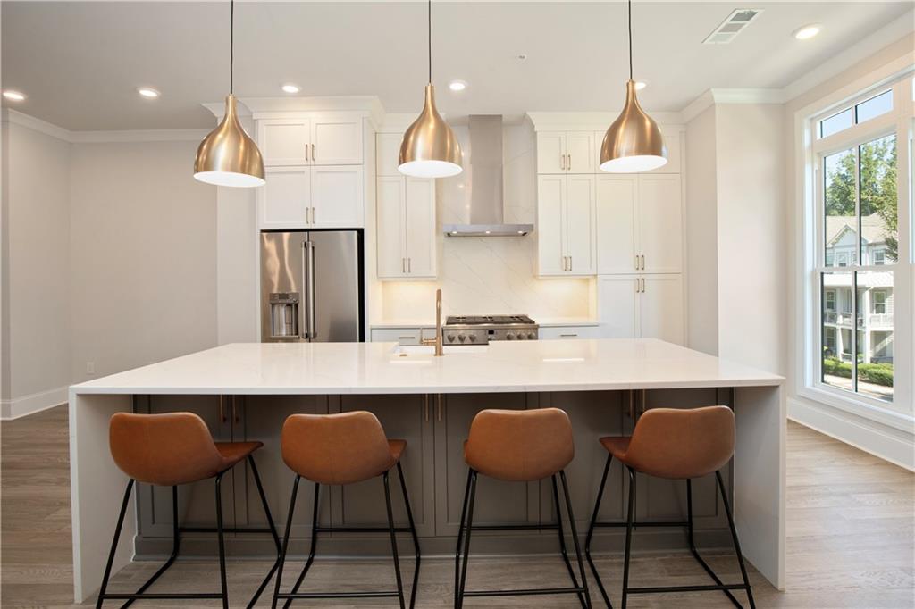 Modern kitchen with a large island, four rust-colored stools, and brass pendant lights.