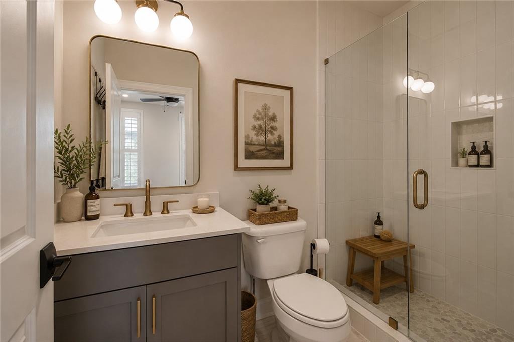 Bathroom with a gray vanity and brass fixtures beside a glass-enclosed shower.