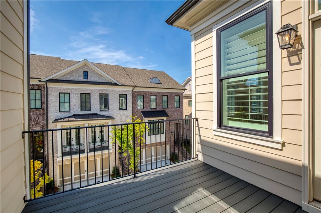 Upper-level balcony with gray decking and black railing overlooking neighboring brick townhomes.