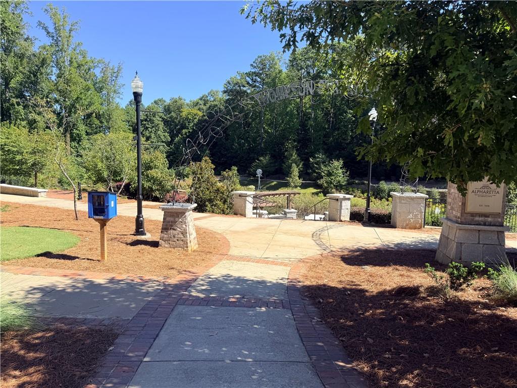Landscaped Alpharetta park entrance with a paved walkway, stone pillars, and an arched sign.