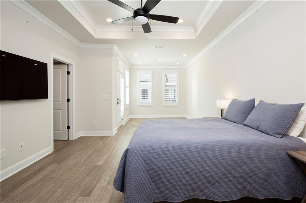 Bedroom with a tray ceiling, ceiling fan, blue-gray bedding, and shuttered windows.