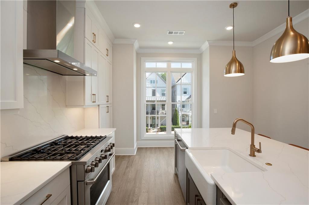 Modern white kitchen with a stainless steel gas range, farmhouse sink, brass fixtures, and a large window.