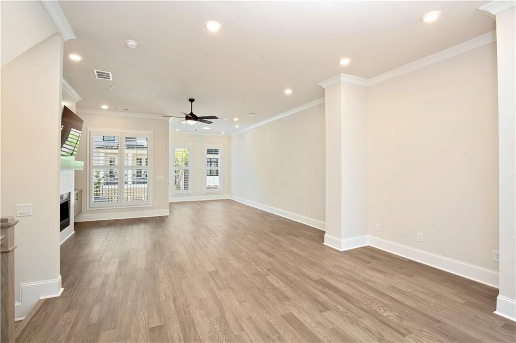 Vacant living room with wide-plank flooring, a ceiling fan, shuttered windows, and a partial fireplace.