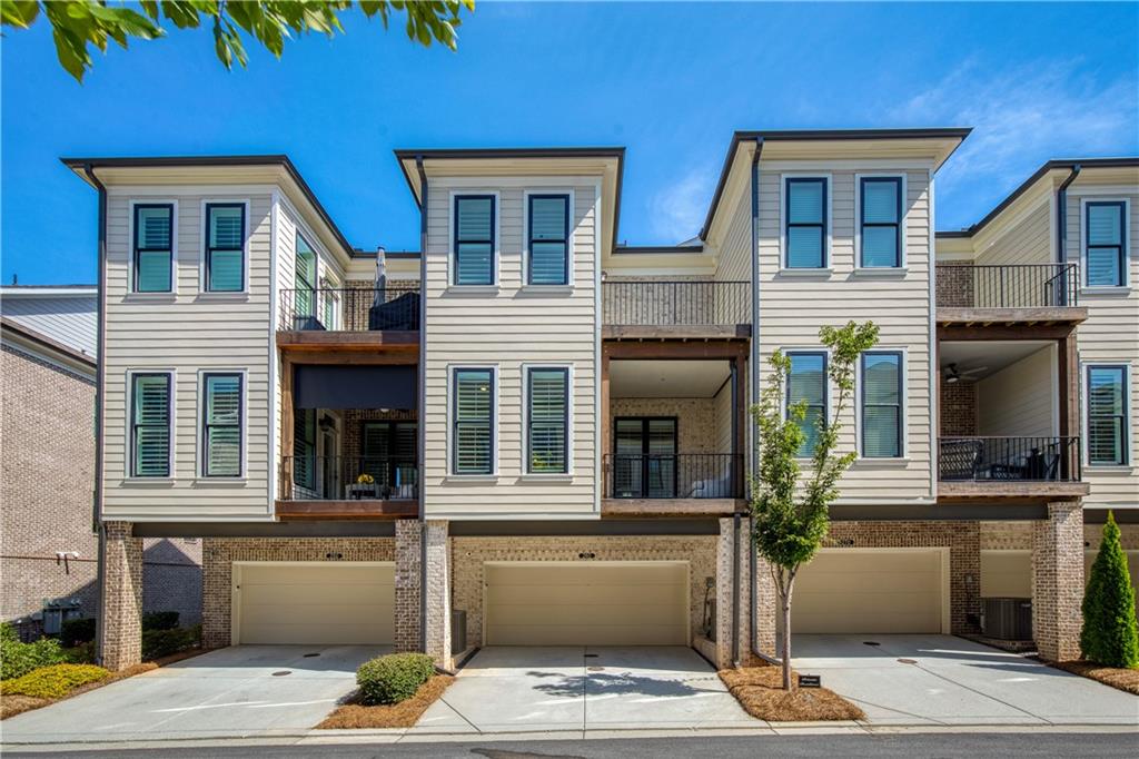 Attached two-story townhomes with balconies, brick lower levels, and private garages.