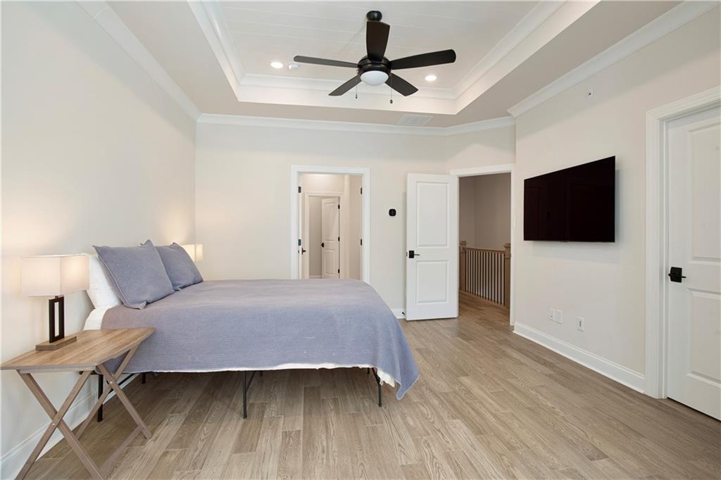Bedroom with pale blue bedding, a tray ceiling, dark ceiling fan, and wall-mounted television.
