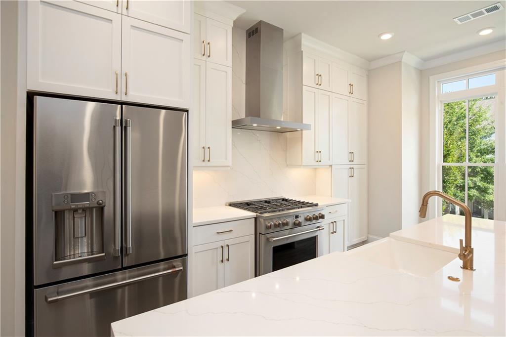 Kitchen with white cabinetry, stainless appliances, and a large island with a brass faucet.