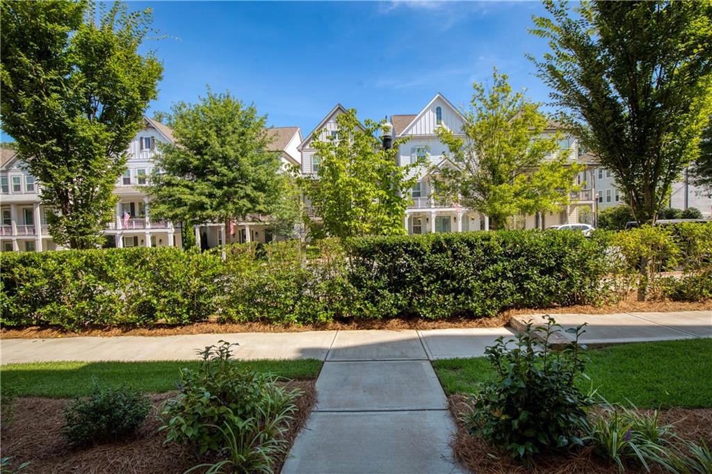 Multi-story townhomes behind a hedge, with a sidewalk leading toward them.