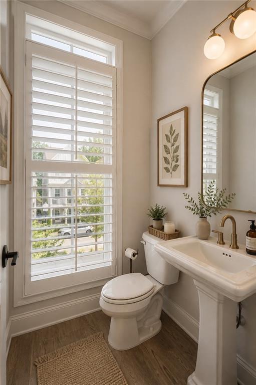 Bathroom with a pedestal sink, toilet, brass fixtures, and a tall shuttered window.