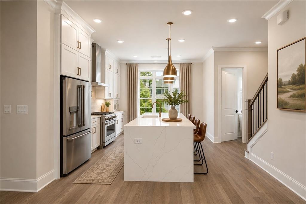 Bright kitchen with a large island, brass pendant lights, and a staircase beside the dining area.