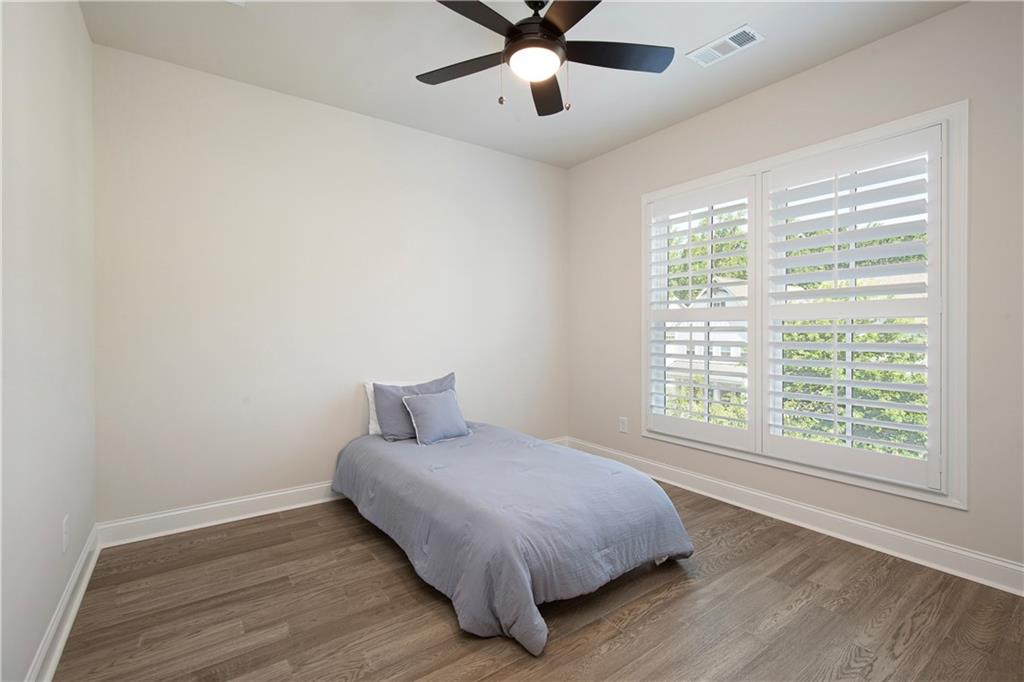 Bedroom with a single bed, wood-look floors, plantation shutters, and a ceiling fan.