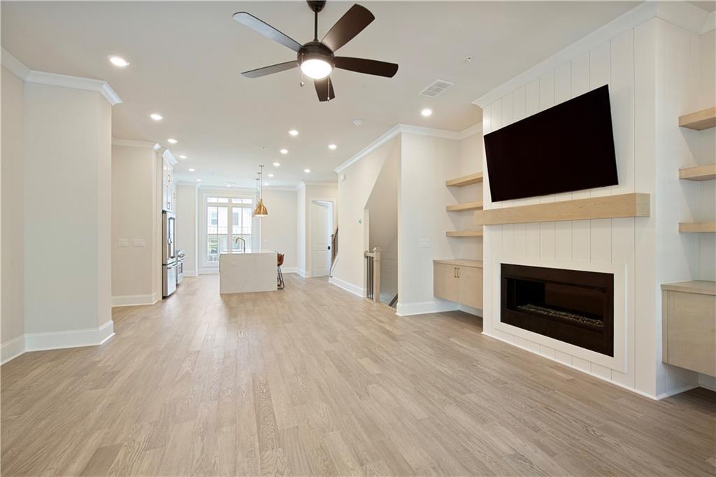 Open-plan living room with a built-in fireplace, wall-mounted TV, and kitchen island beyond.
