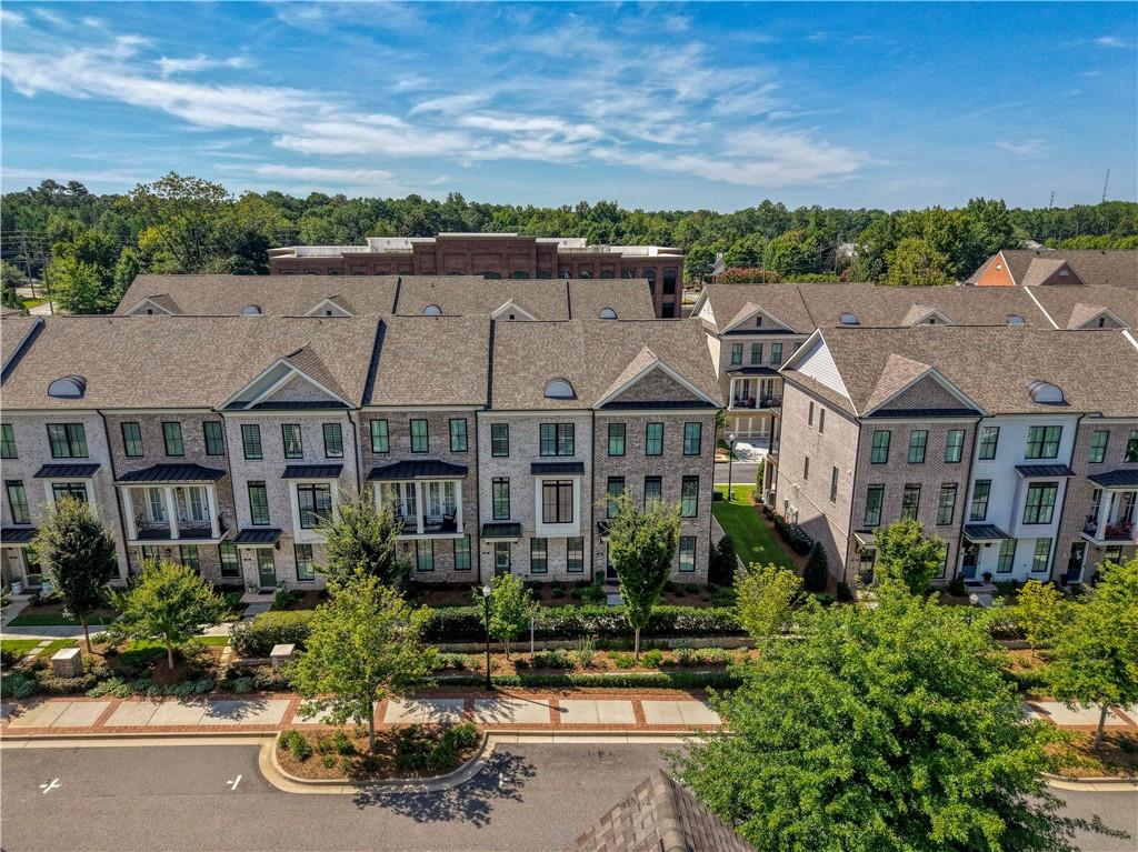 Aerial view of multi-story townhomes with gray roofs along a landscaped sidewalk.