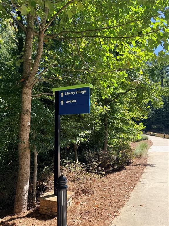 Directional sign for Liberty Village and Avalon beside a shaded, landscaped sidewalk.