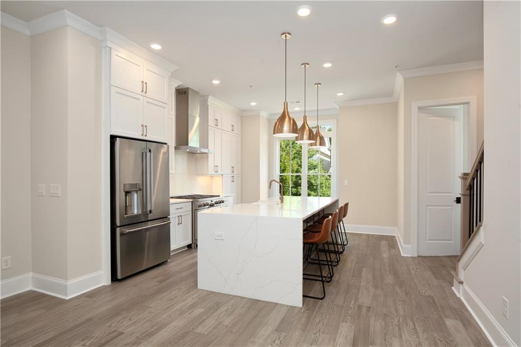 Modern kitchen with a white waterfall island, brown bar stools, and brass pendant lights.