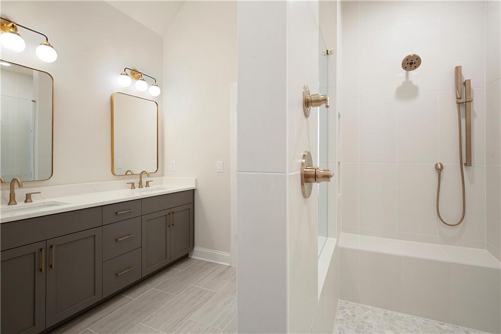 Bathroom with a dark double vanity, brass-framed mirrors, and a white-tiled shower.