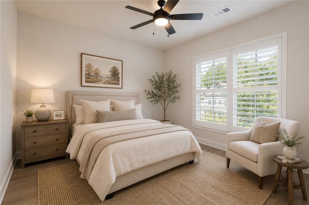 Bright staged bedroom with neutral bedding, plantation shutters, and an upholstered armchair.