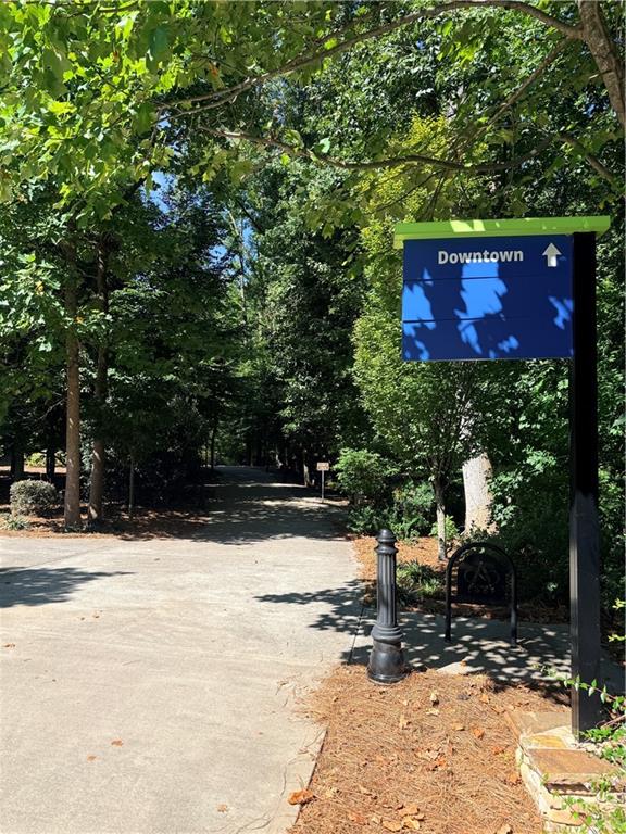 Tree-lined paved walkway with a blue Downtown sign and a black metal bench.