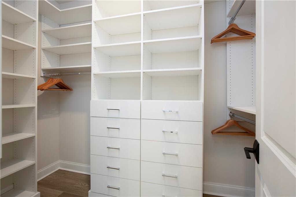 Walk-in closet with white built-in shelves and drawers, hanging rods, and wood flooring.