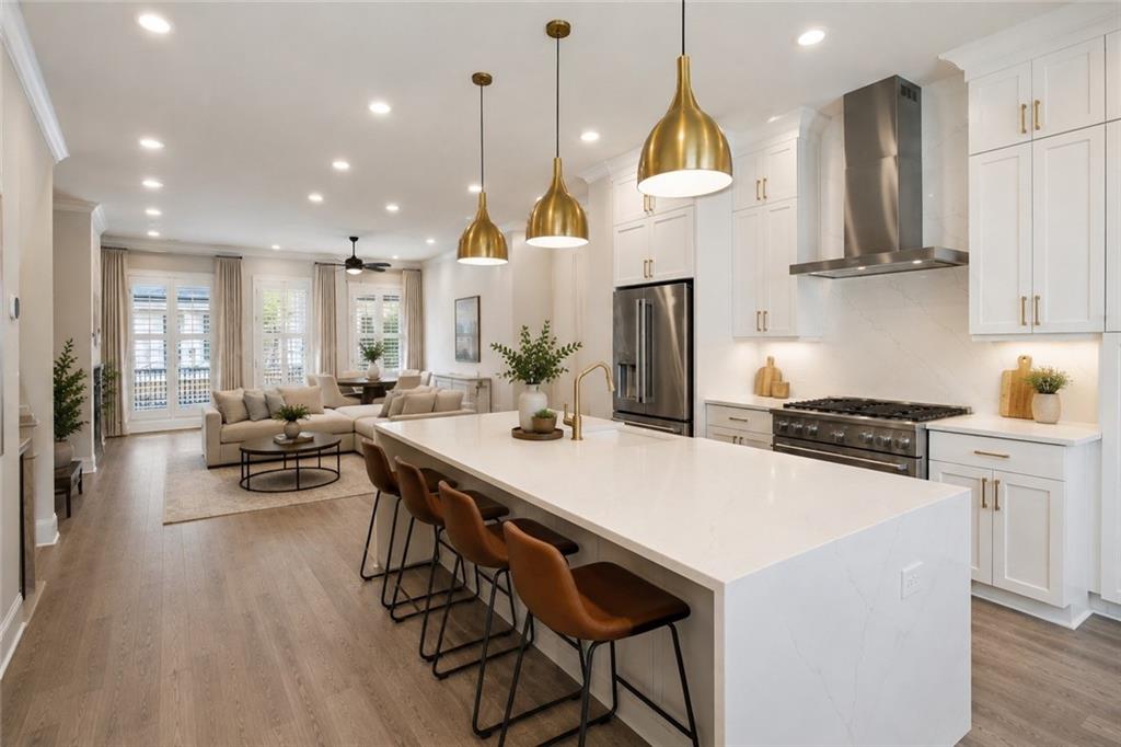 Open-plan kitchen with a large white island, brass pendants, and an adjoining living area.