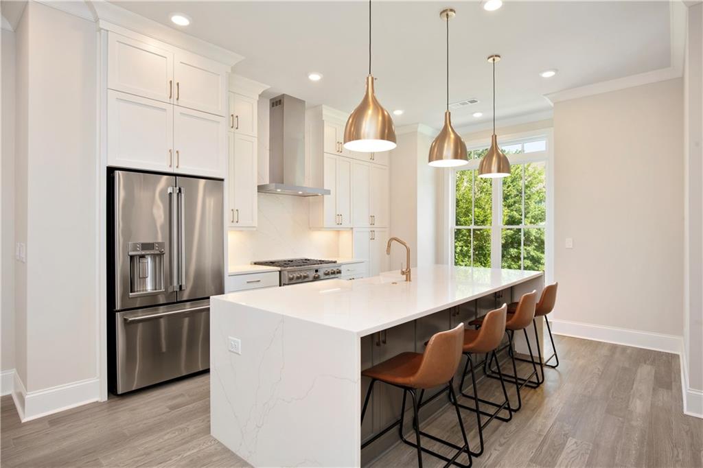 Modern kitchen with a large white waterfall island, brass pendant lights, and a tall window overlooking greenery.