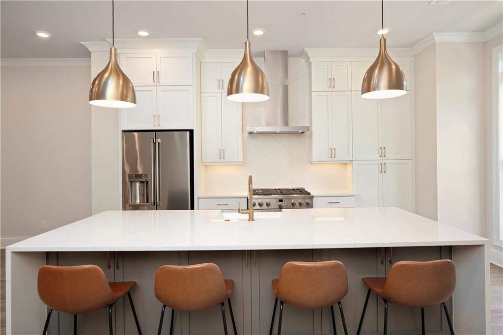 Bright kitchen with a large white island, four stools, stainless appliances, and brass pendant lights.