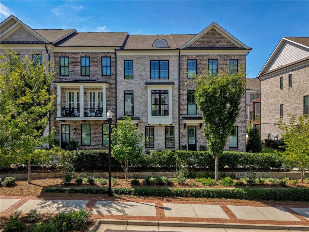 Brick townhouse with small balconies and landscaped frontage beside a sidewalk.