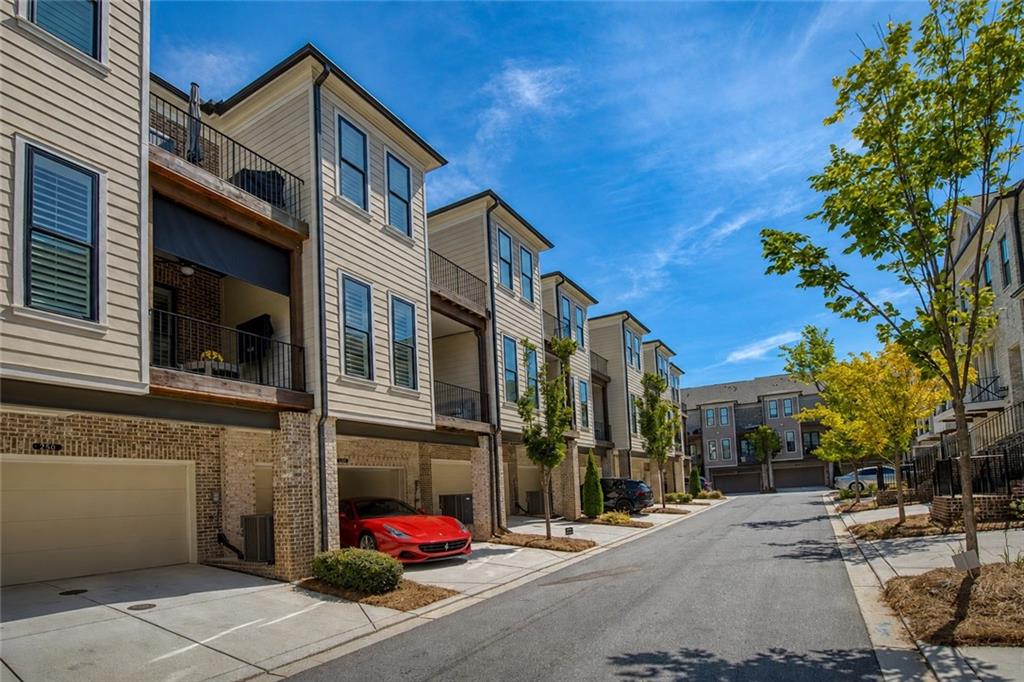 Townhouses line a sunny street, with balconies, garages, and a red sports car in a driveway.