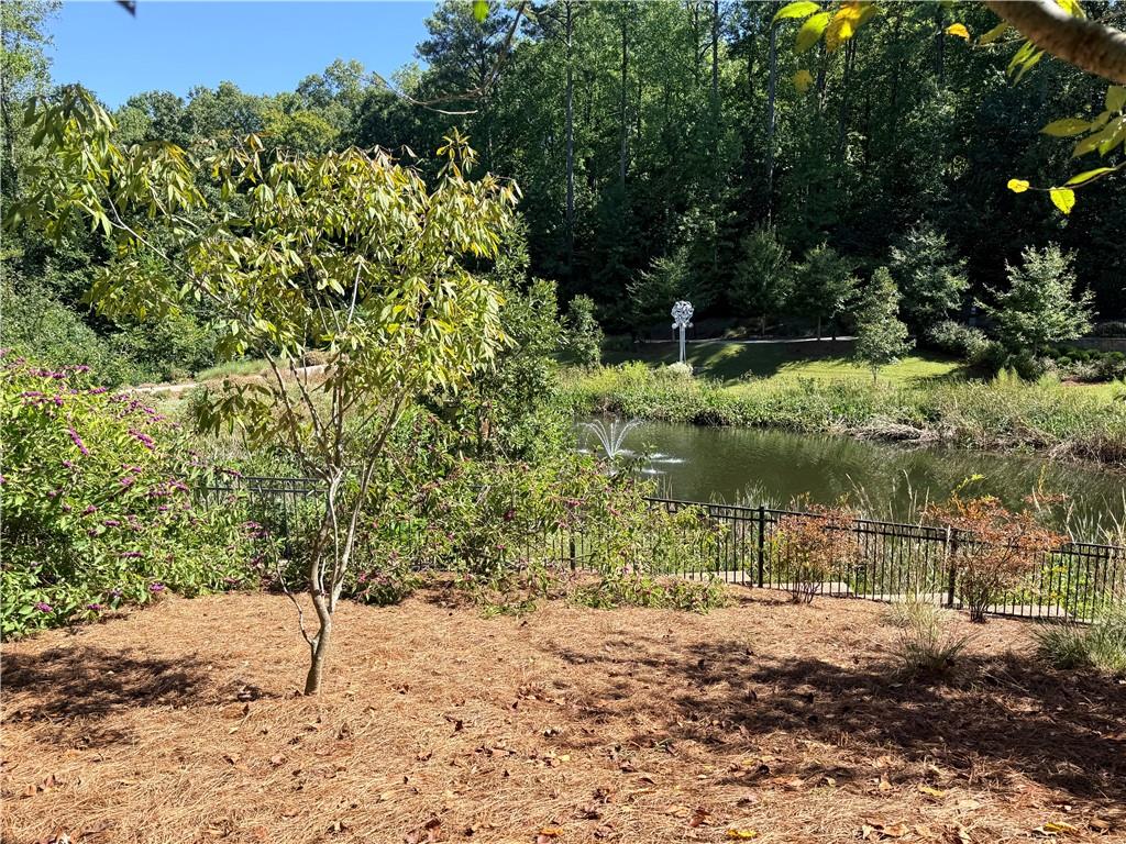 Landscaped backyard pond with a small fountain, black metal fence, and mature trees.