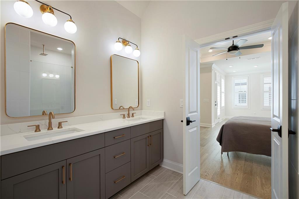 Bathroom with a double-sink gray vanity and brass fixtures, opening into a bedroom.