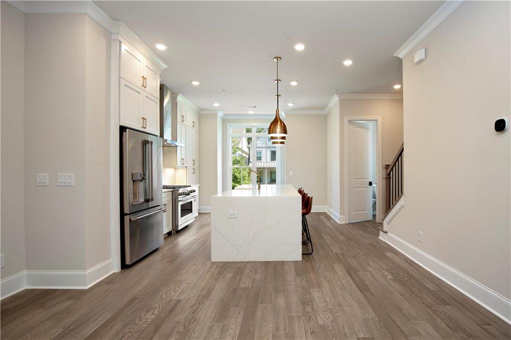 Modern kitchen with white cabinets, stainless steel appliances, and a large island beneath pendant lights.