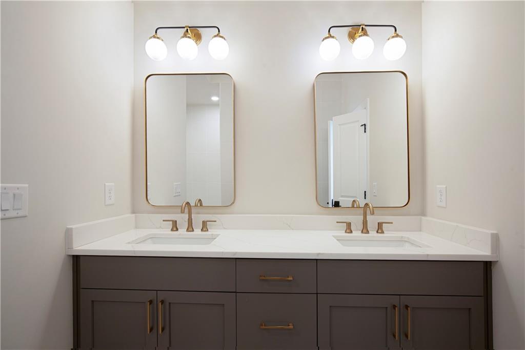Bathroom double vanity with gray cabinets, brass faucets, and two gold-framed mirrors.
