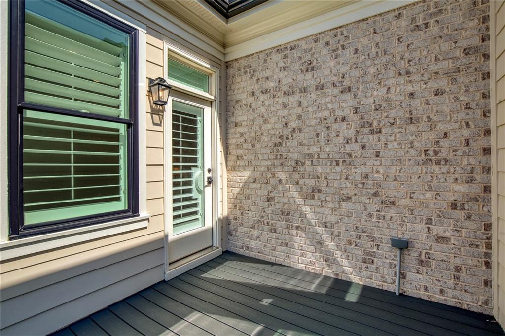 Covered porch with dark decking, a shuttered glass door, and light brick walls.