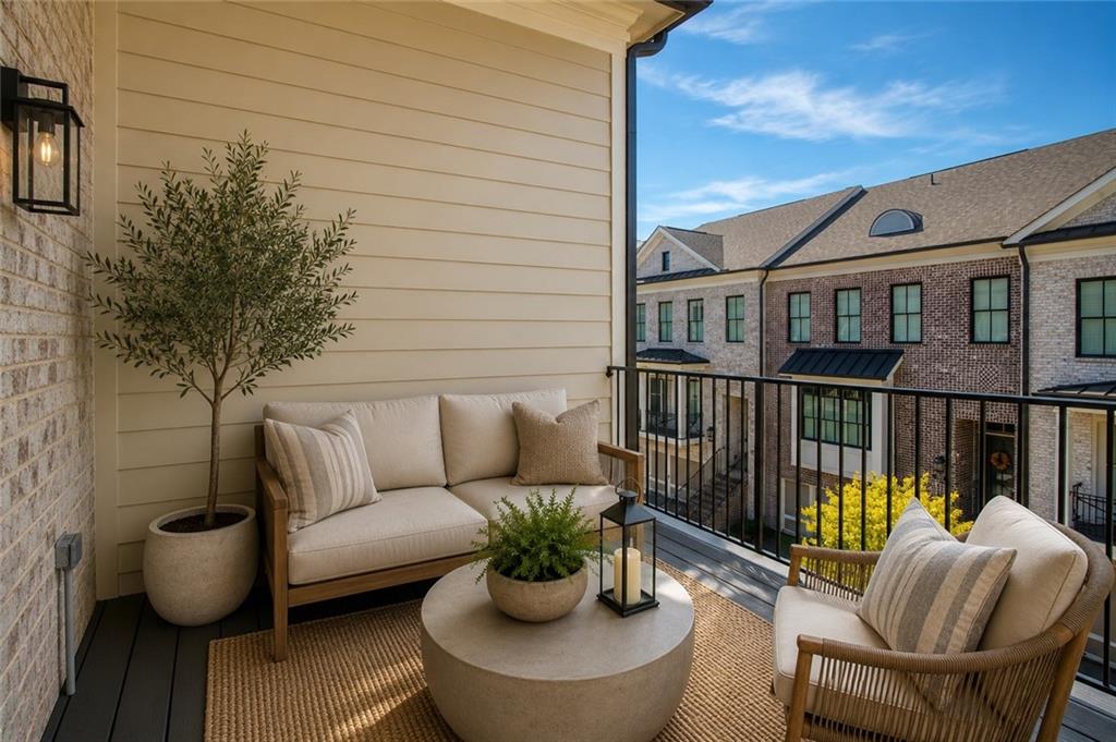 Furnished balcony with cushioned seating and potted plants overlooking neighboring brick townhomes.
