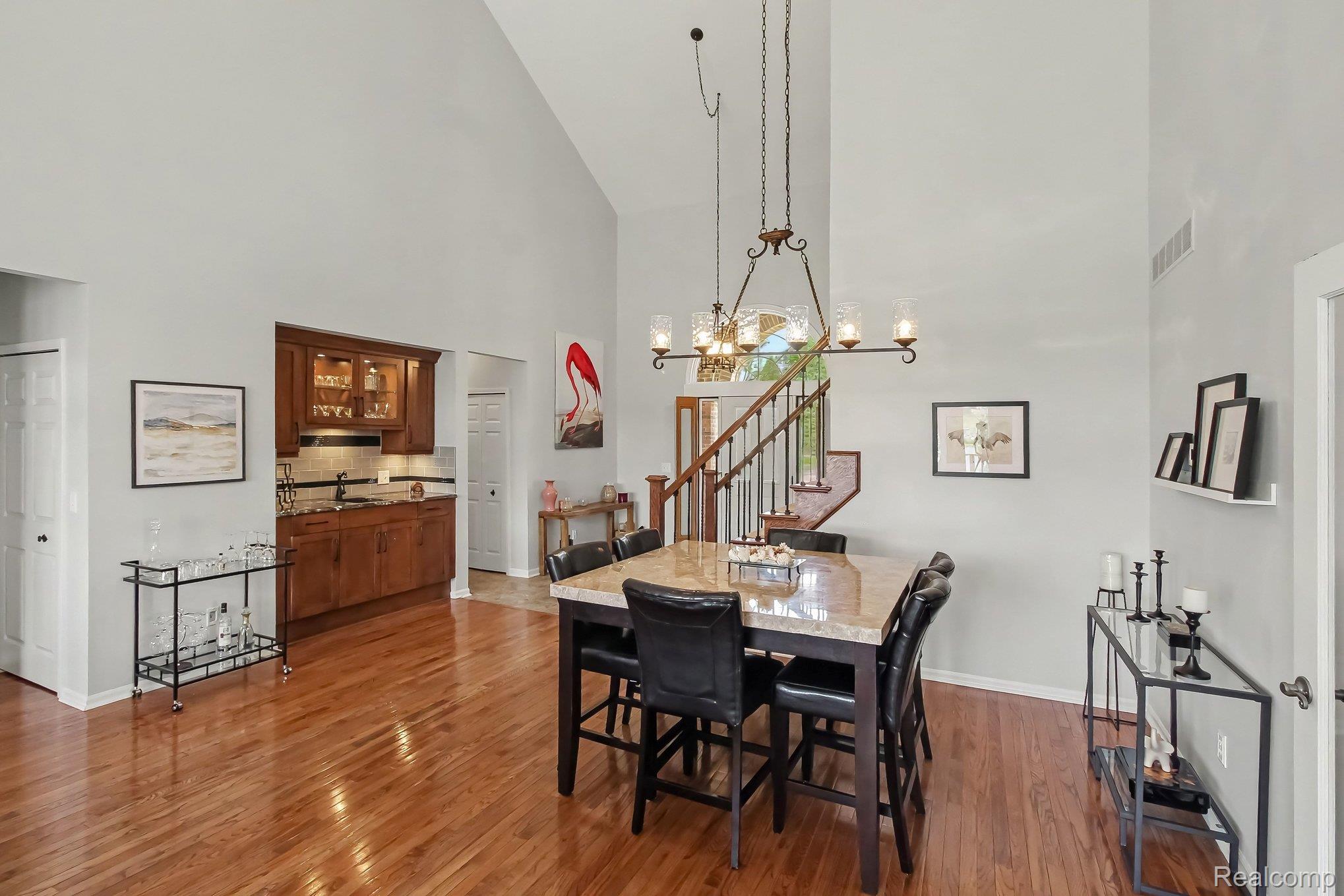 Dining room with a stone-top table, hardwood floors, and a staircase beneath a tall arched window.
