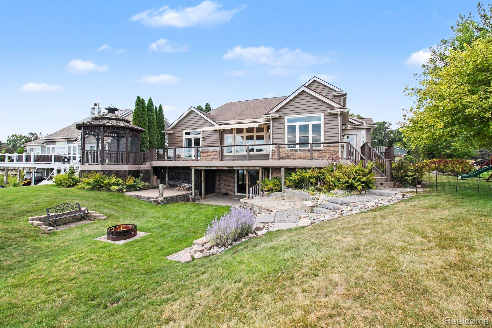 Home’s rear deck and gazebo overlook a landscaped lawn with a stone path and fire pit.