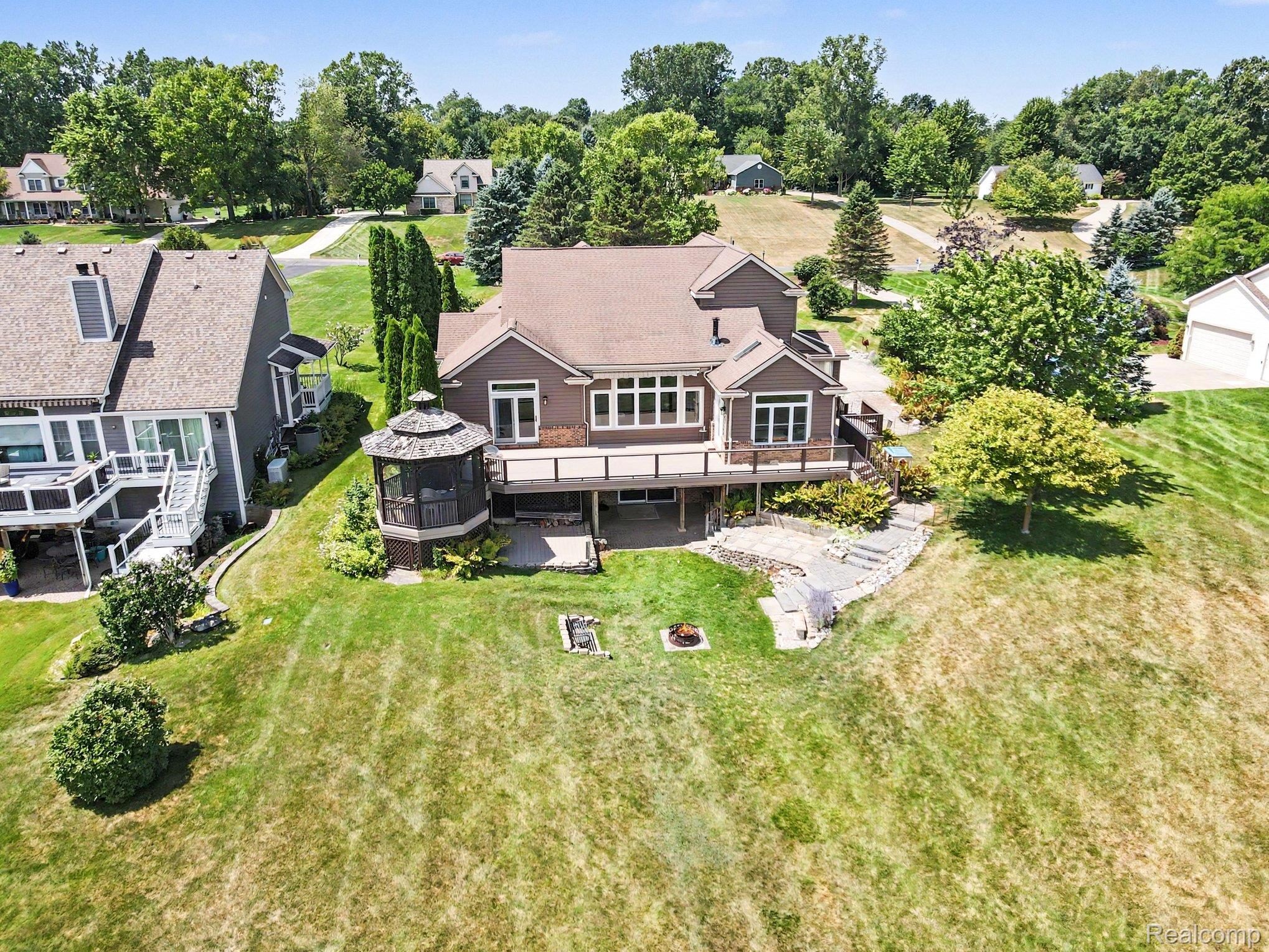 Rear of a brown house with a long deck, gazebo, stone steps, and a broad grassy yard.