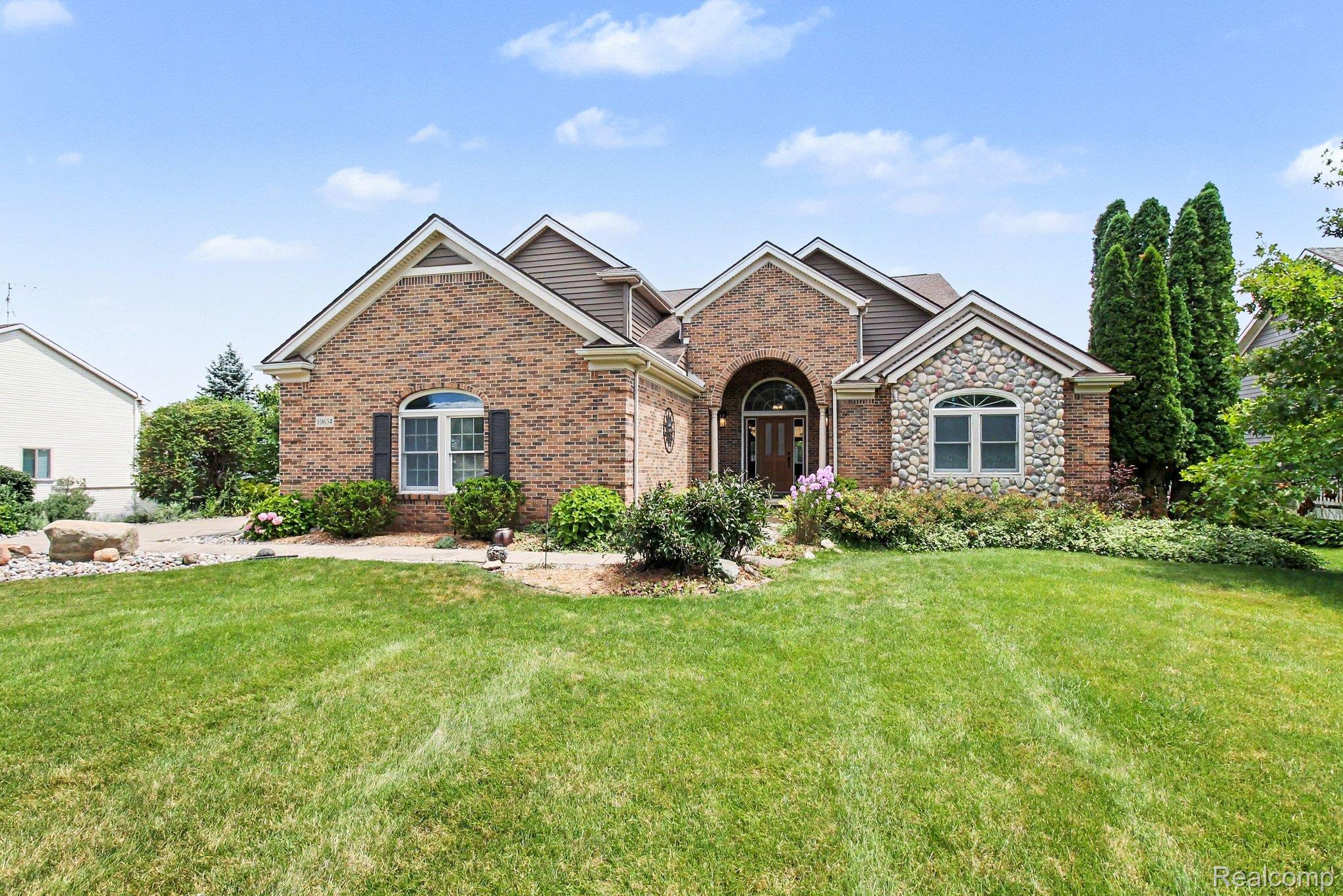Brick house with a stone facade section, arched entry, and landscaped front lawn.