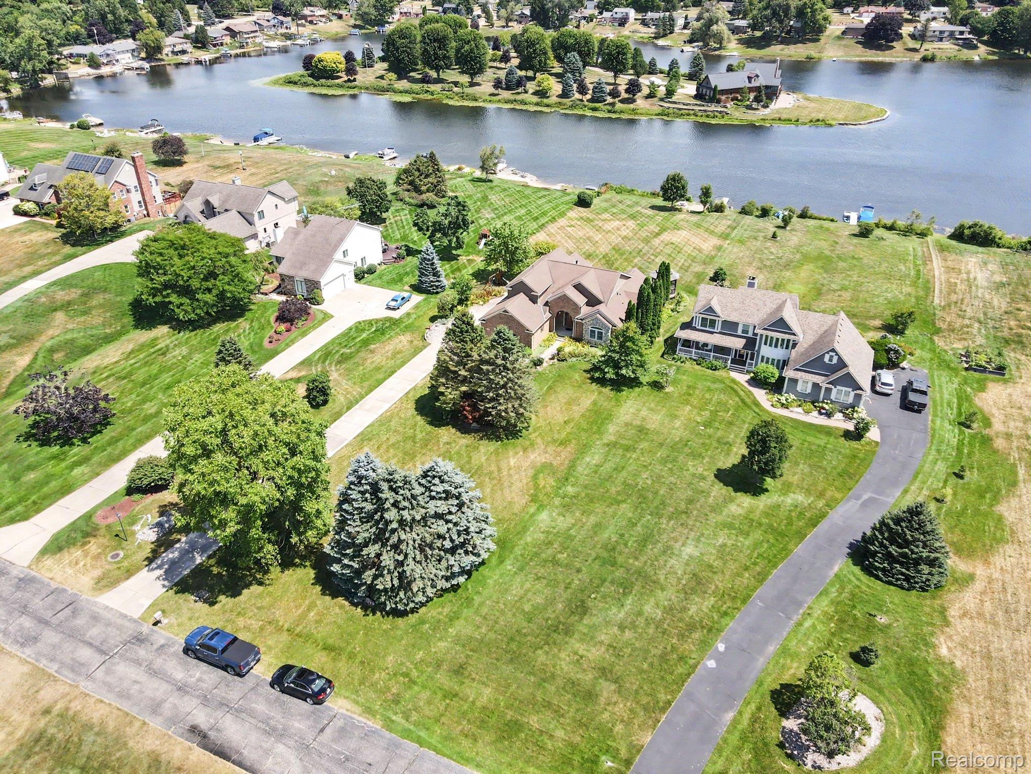 Aerial view of a home on a large lawn beside a waterway and neighboring houses.