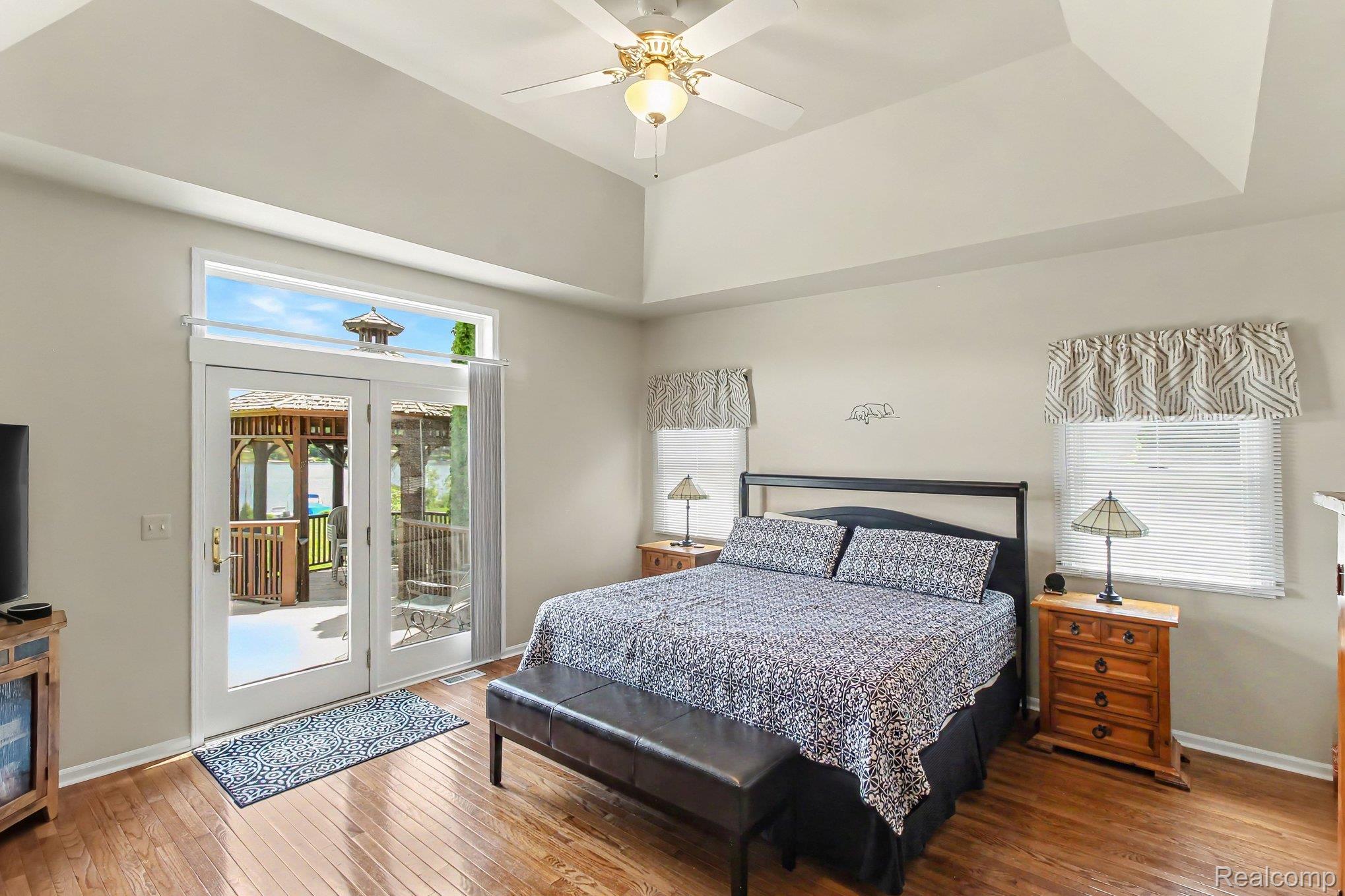 Bedroom with a vaulted ceiling, patterned king bed, and glass doors opening to a deck overlooking water.