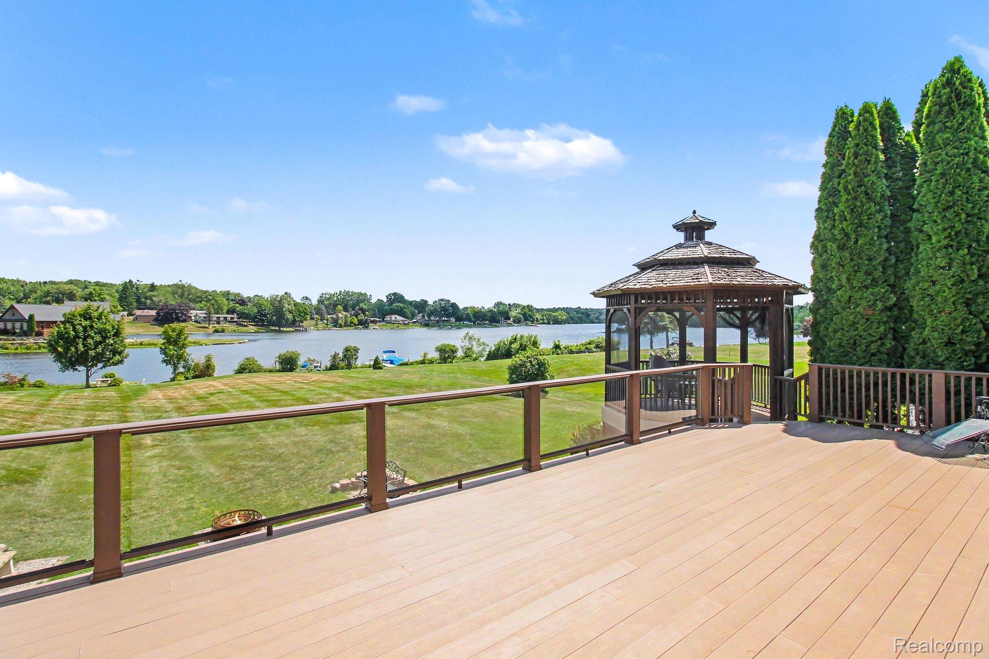 Spacious deck and gazebo overlook a lawn and lake.