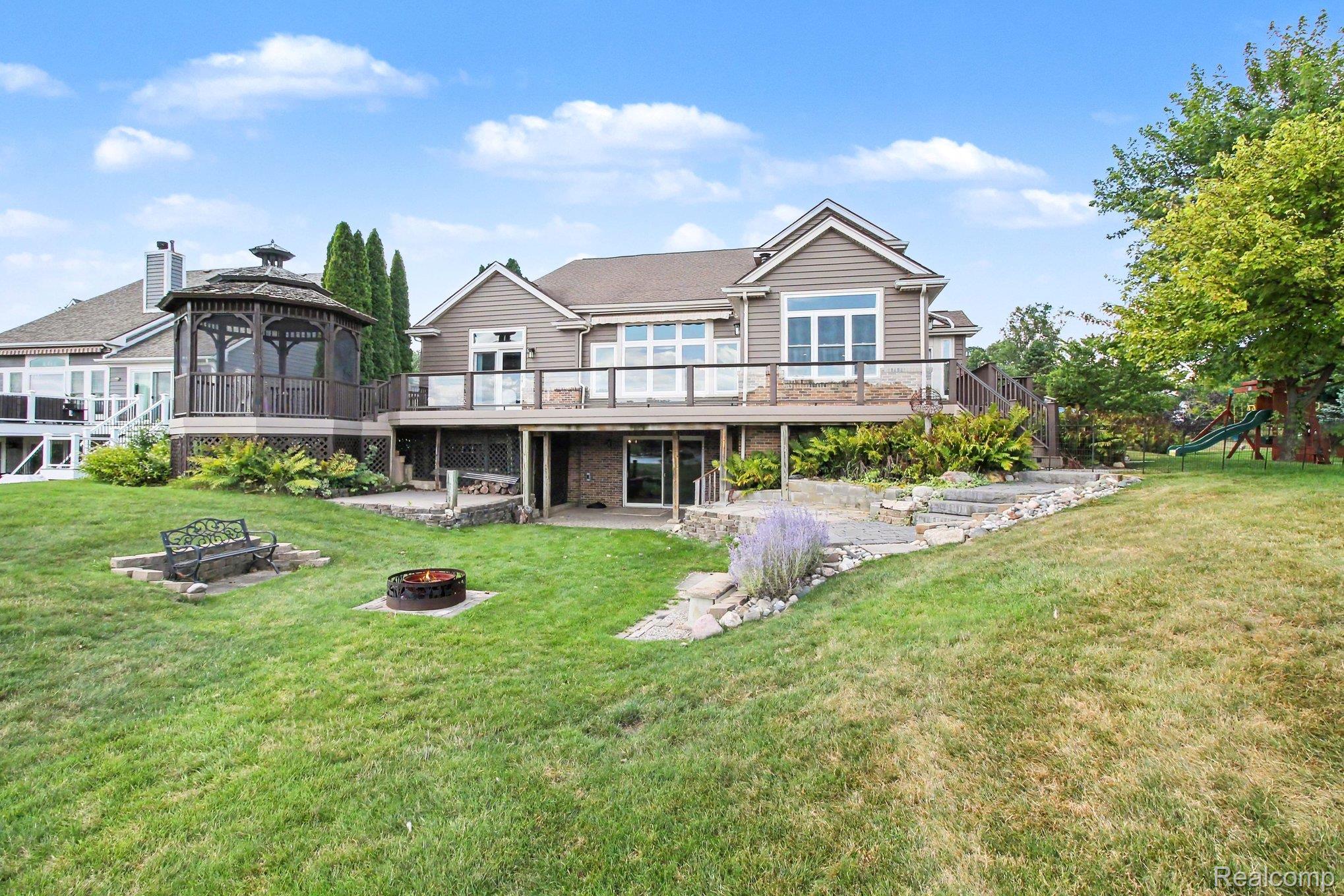 Home’s rear deck and screened gazebo overlook a landscaped lawn with a fire pit and playset.
