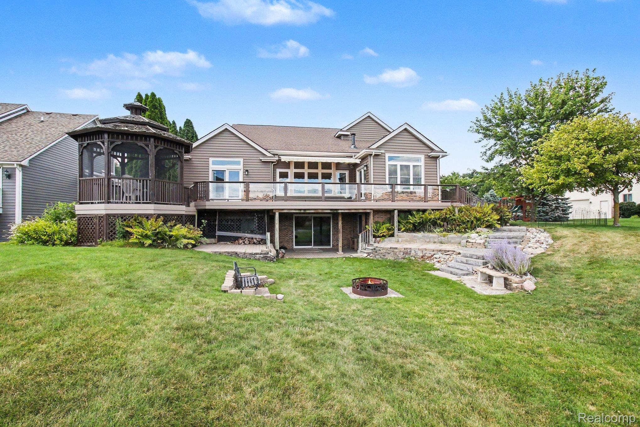 Home’s rear deck and screened gazebo overlook a landscaped lawn with stone steps and a fire pit.